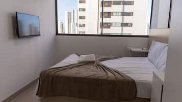 A hotel room with a bed, a bedside table, a TV mounted on the wall, and a window with a view of buildings.