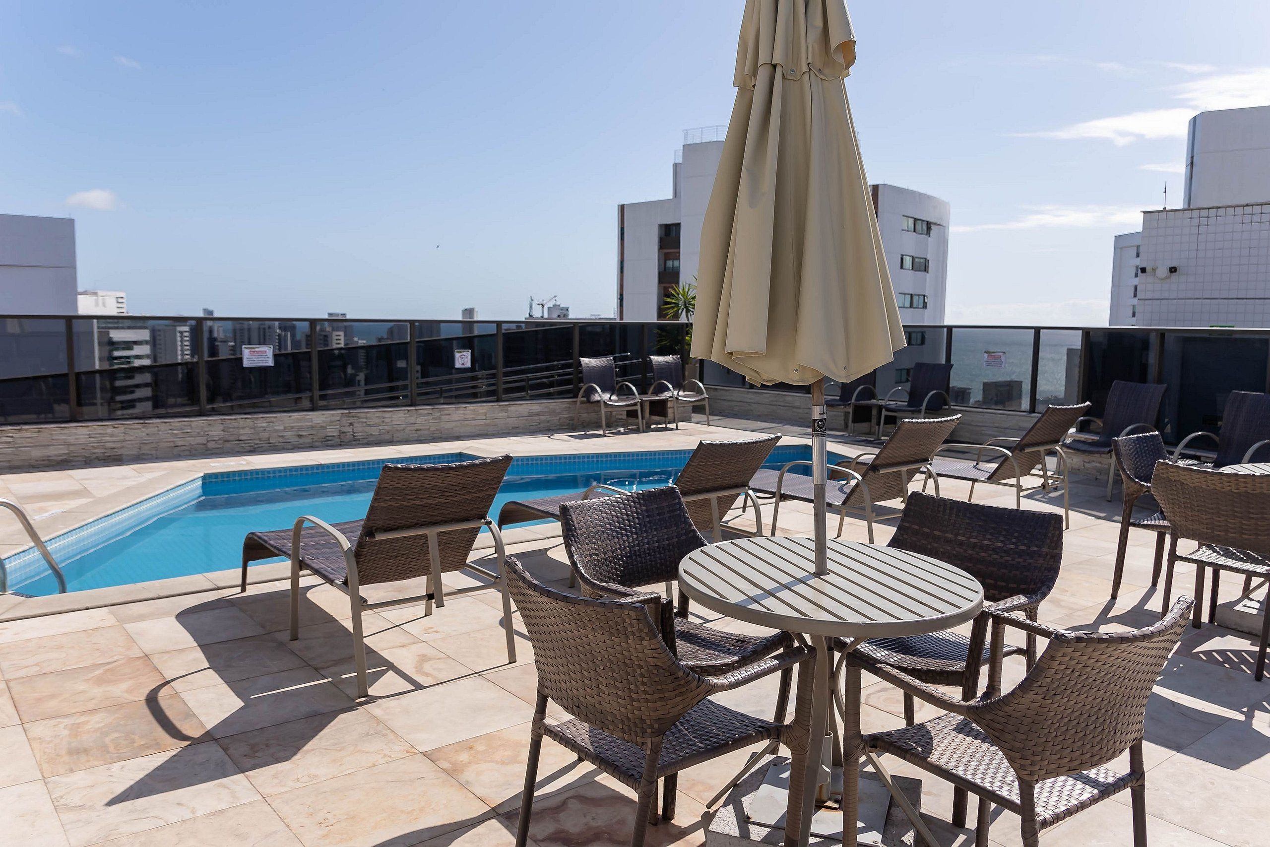 Un espace piscine aménagé sur le toit, avec des fauteuils et des tables en osier, une piscine et une vue sur le paysage urbain.
