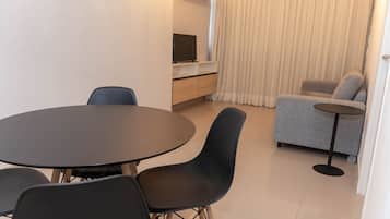 Un salon moderne avec une table ronde et des chaises, un canapé, un téléviseur posé sur une étagère et un rideau.
