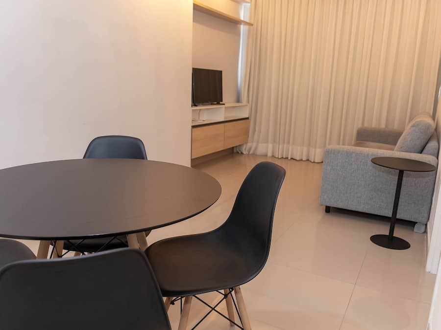 Una sala de estar moderna con una mesa redonda y sillas, un sofá, un televisor en un estante y una cortina.