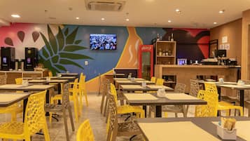 Un restaurante con varias mesas y sillas, un televisor montado en la pared y un refrigerador de Coca-Cola.