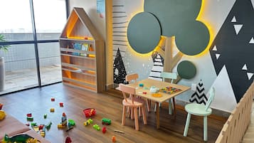 A children's playroom with a wooden bookshelf, a table with toys, and a wall with geometric decorations.