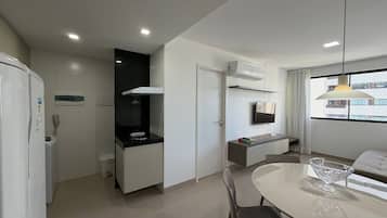 A modern kitchen with a built-in oven, a microwave, and a coffee machine. There is a dining area with a table and chairs, and a window with a view of buildings.
