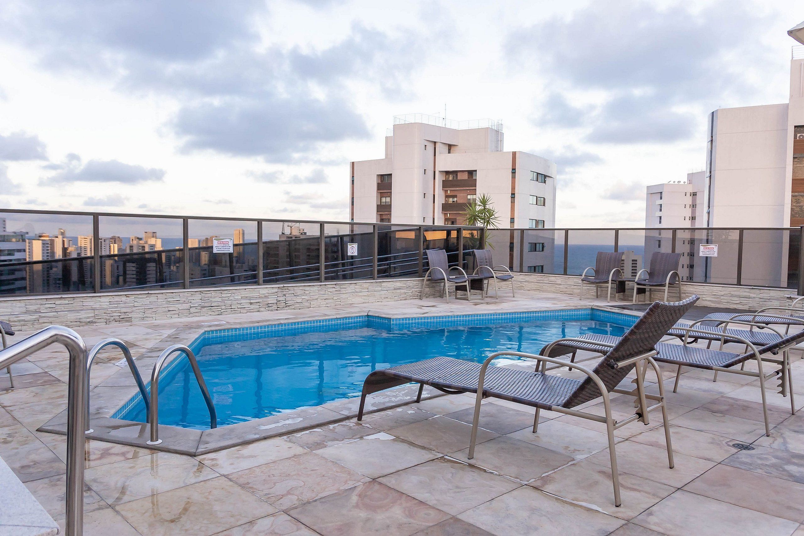 A rooftop pool with lounge chairs, a clear view of the cityscape, and a modern building in the background.
