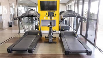 A gym with treadmills, a stationary bike, and a TV screen on the wall.