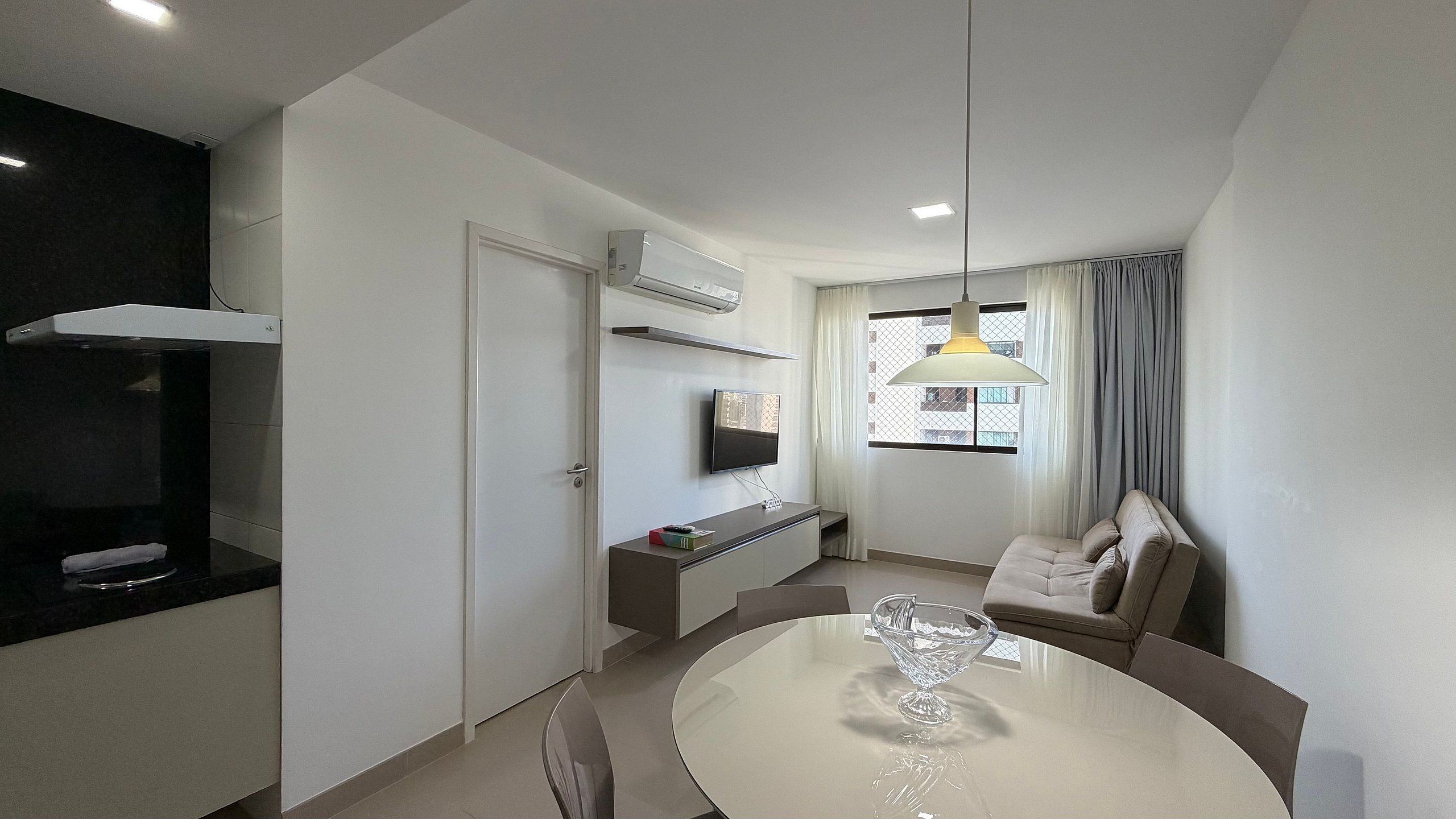 A modern living room with a dining table, sofa, and a TV mounted on the wall.