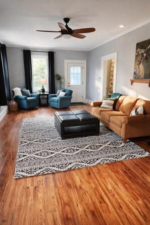 A living room with a ceiling fan, two blue armchairs, a brown sofa, a patterned rug, and wooden flooring. - State Ave|Central AC|Beach 400ft (Alpena)