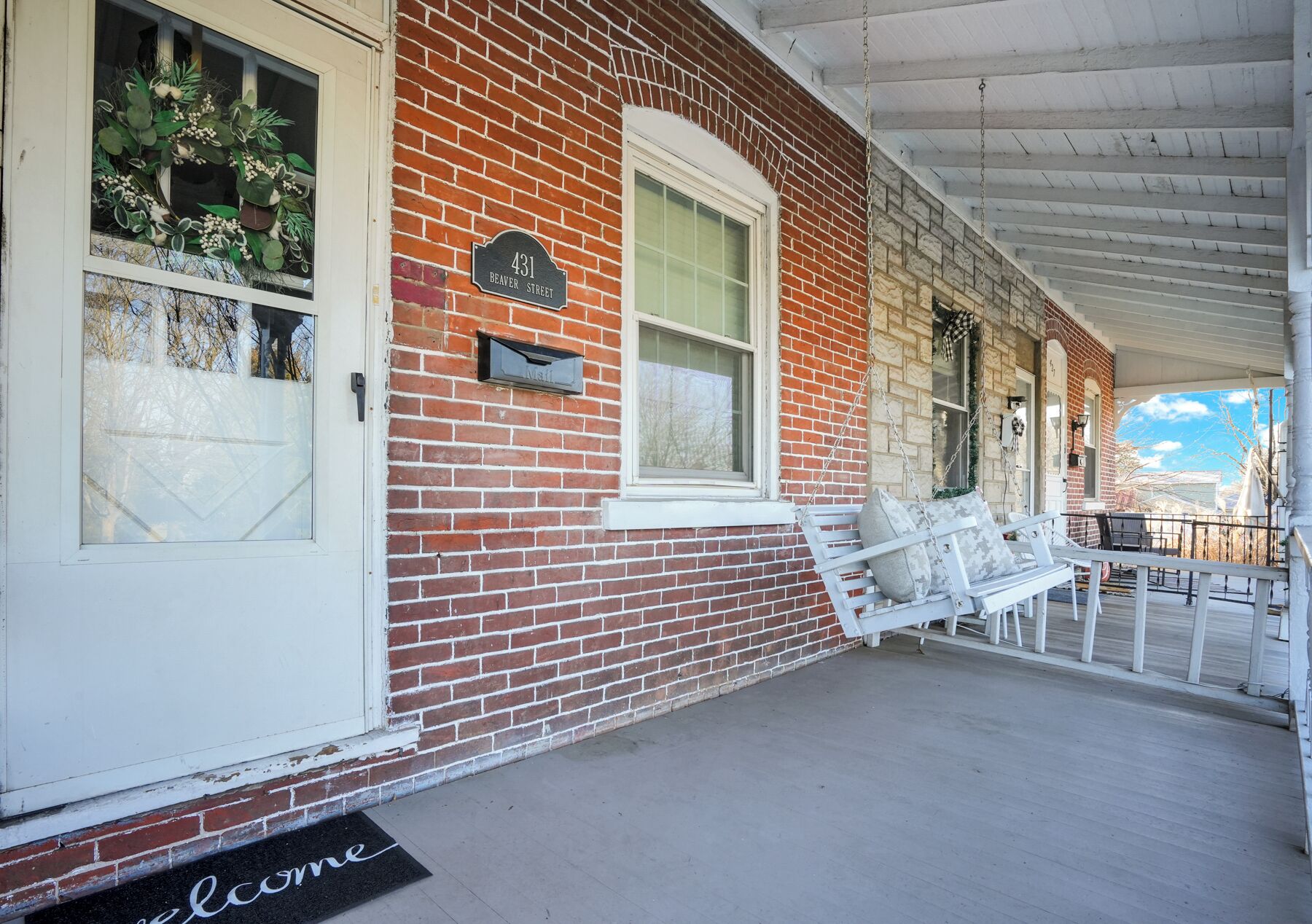 A red brick building with a white porch, a mailbox, and a welcome mat.