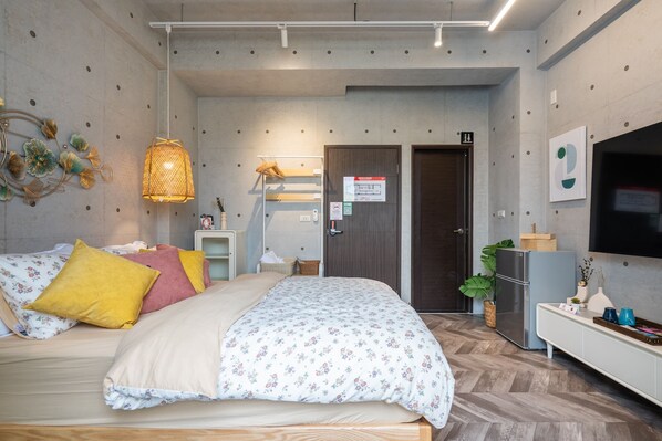 Moderni hotellihuone, jossa on sänky, televisio, jääkaappi ja huonekasvi.
