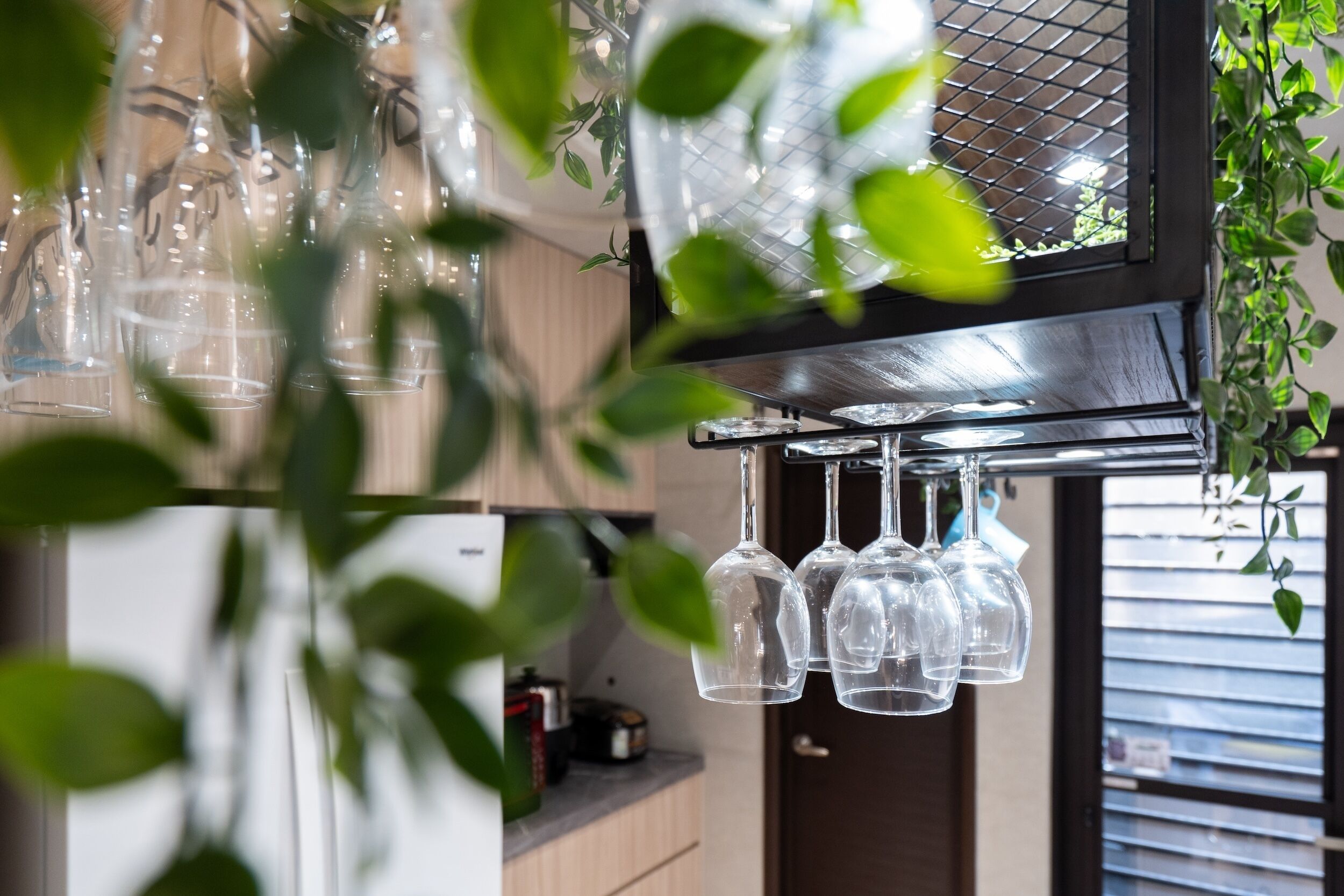 A kitchen with hanging wine glasses and a window with blinds.