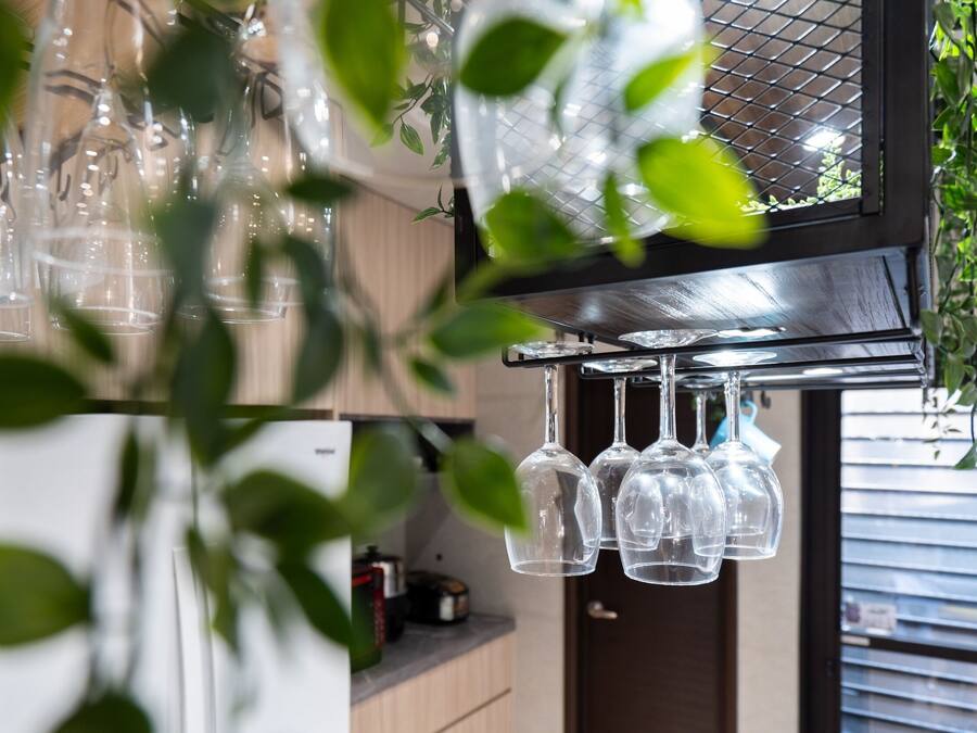 A kitchen with hanging wine glasses and a window with blinds.