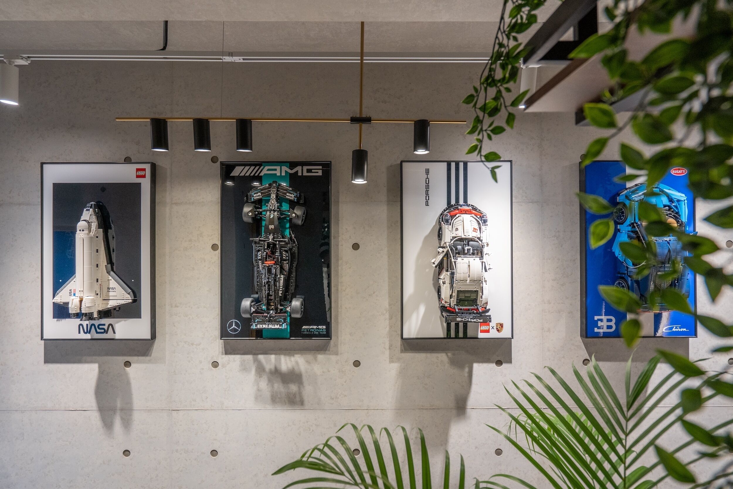 Four framed posters on a wall, each depicting a different vehicle: a space shuttle, an AMG car, a Porsche car, and a Formula 1 car.