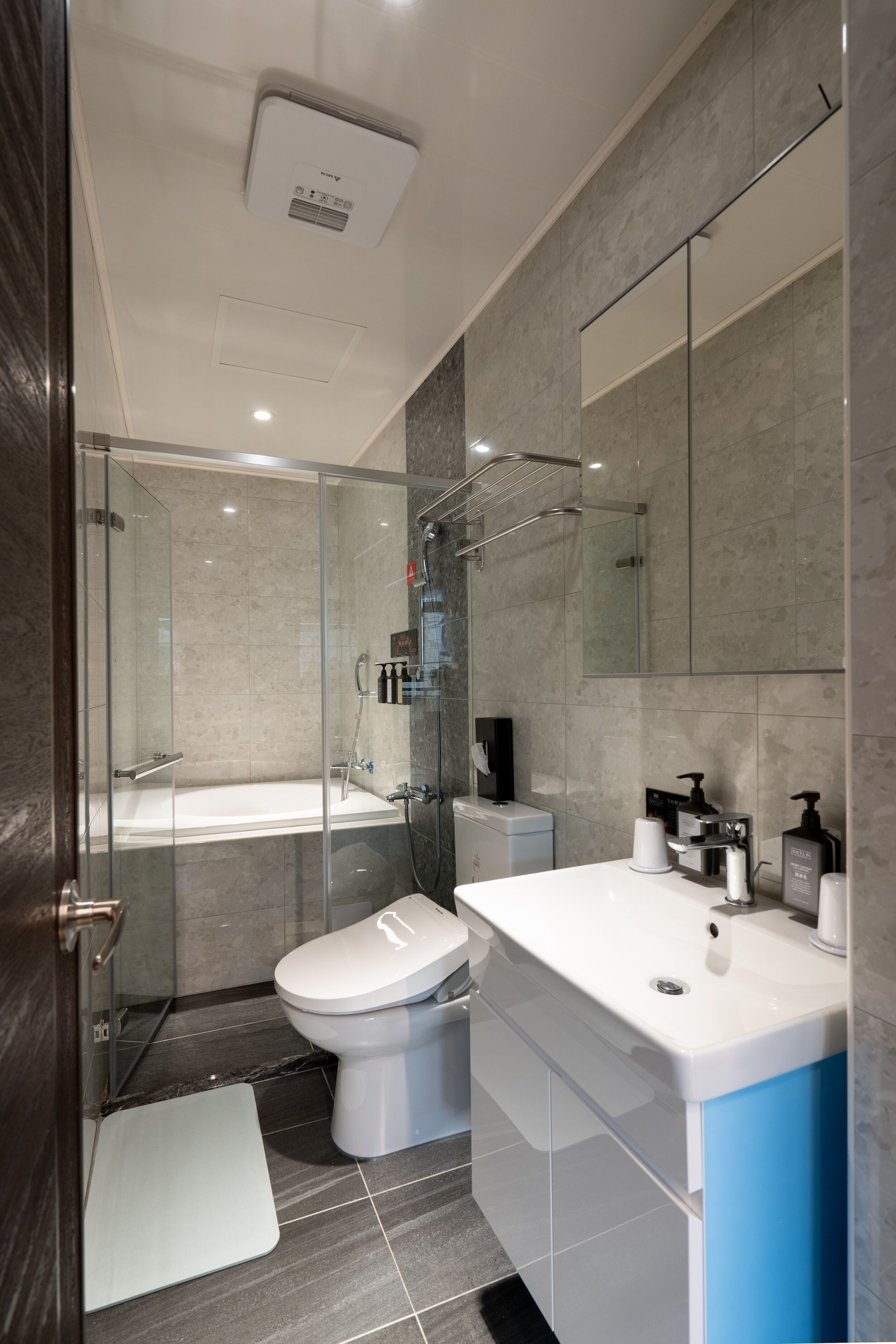 A modern bathroom with a glass-enclosed shower, a white toilet, a large white sink, and a mirror above the sink.