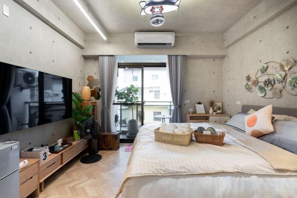 A modern bedroom with a large bed, a flat-screen TV, a desk, and a window with curtains.