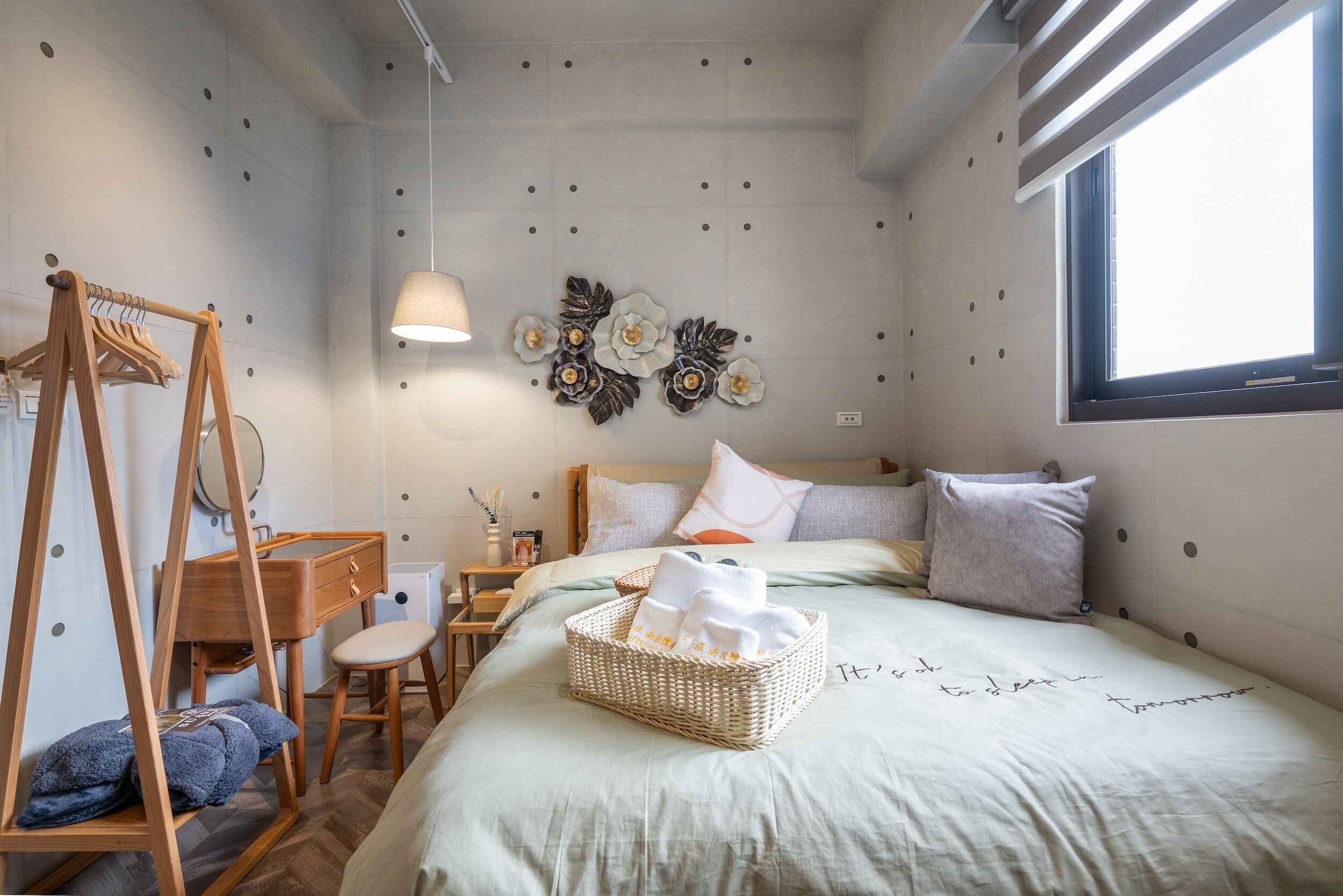 A bedroom with a bed, a wooden wardrobe, a desk, a hanging light, and wall decorations.