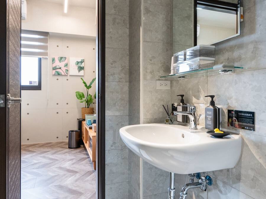 A modern bathroom with a large sink, mirror, and a door leading to a hallway with a herringbone floor and a plant.