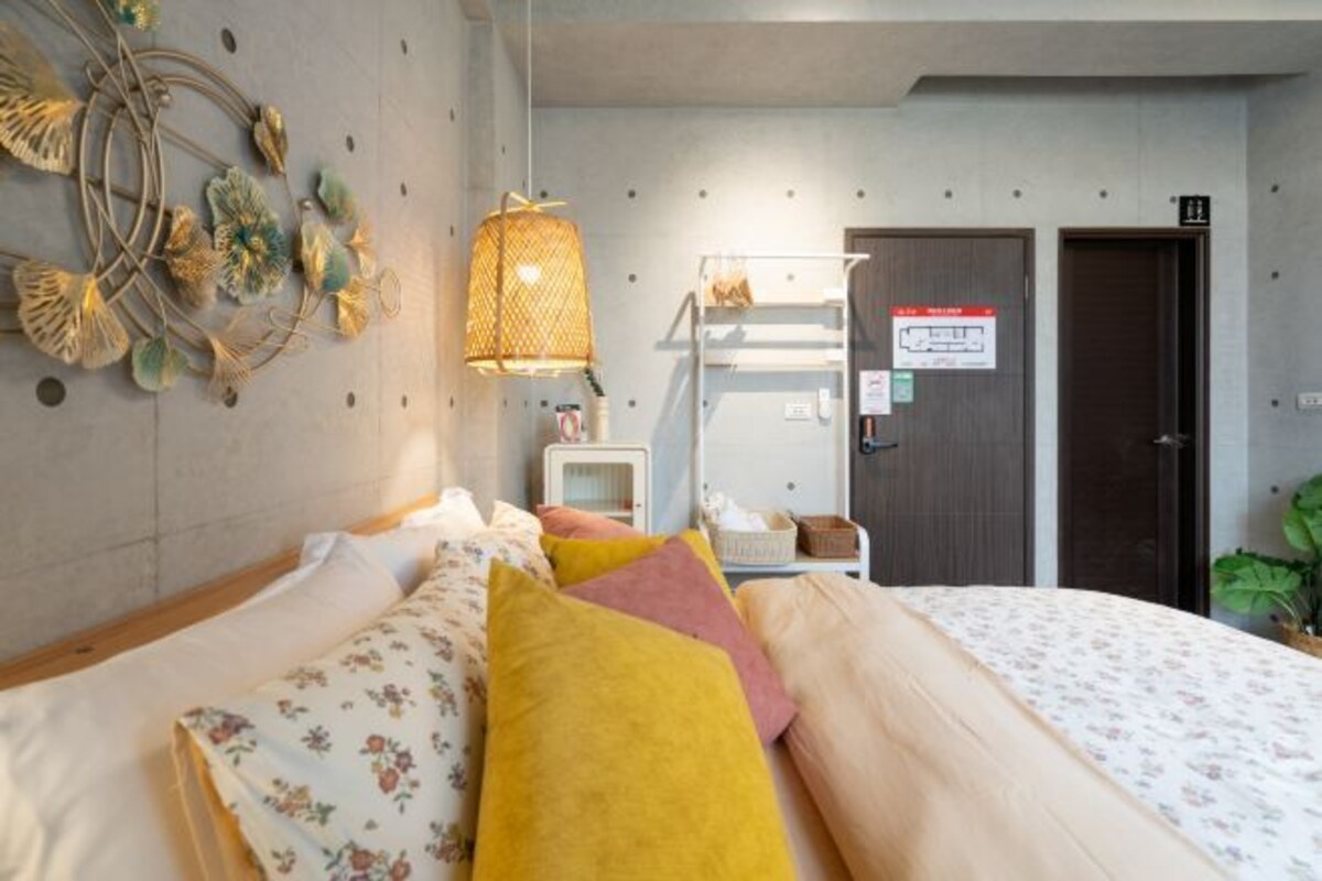 A hotel room with a bed, a bedside table, a lamp, a mirror, and a door.