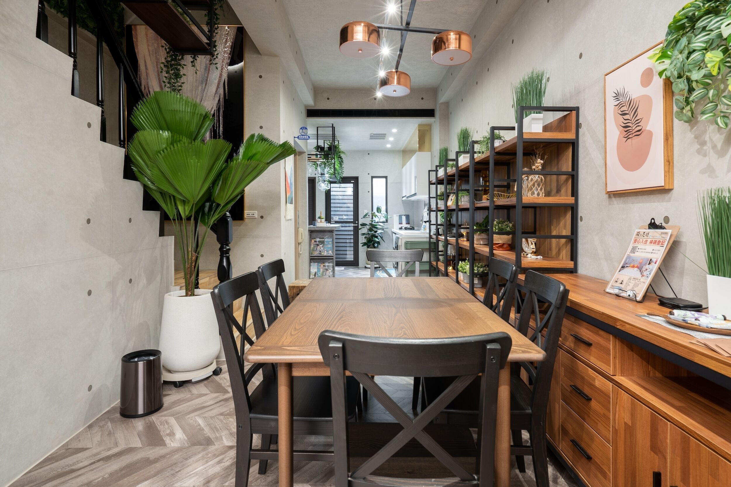 A modern dining area with a wooden table and black chairs, surrounded by shelves with plants and decorative items.