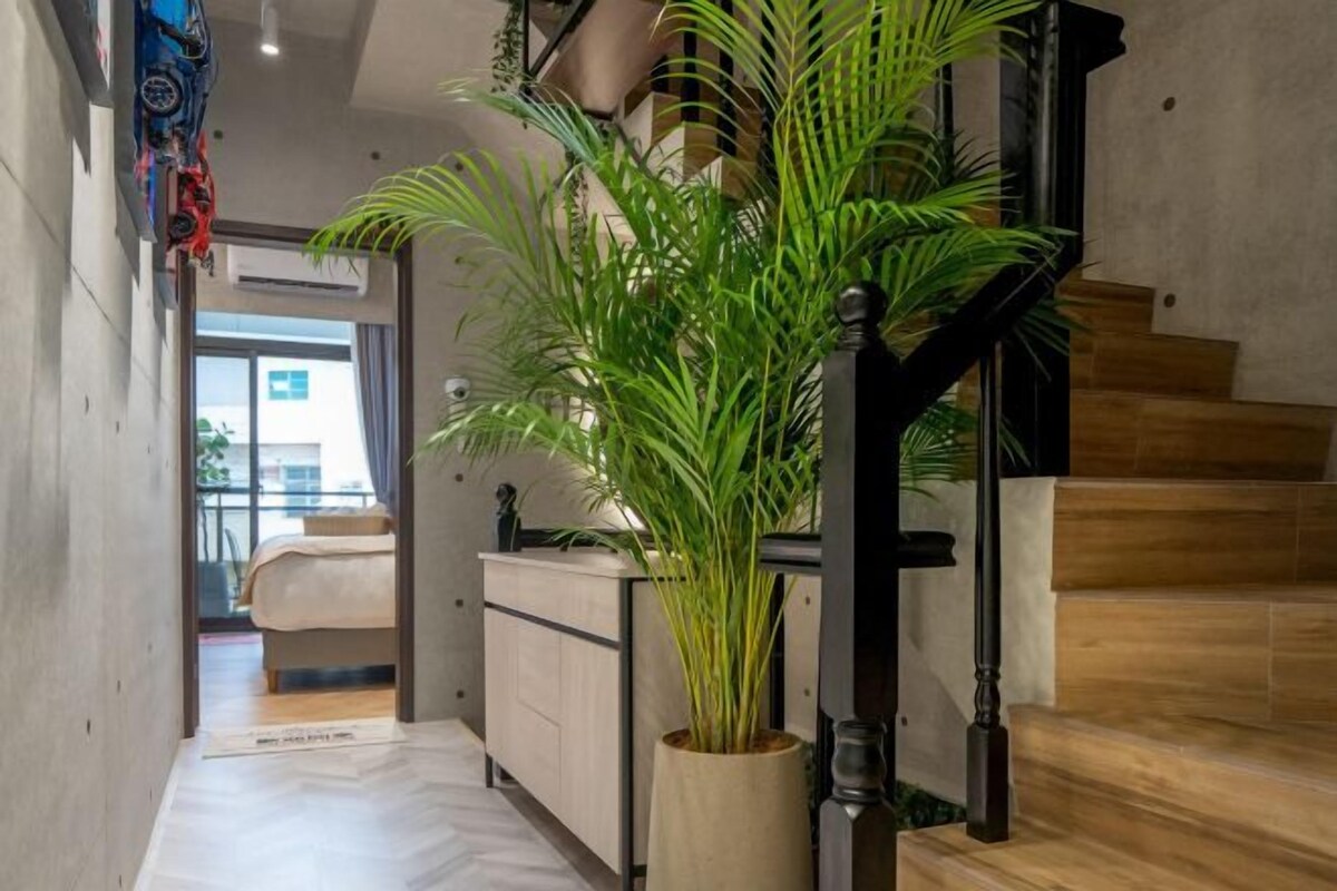 A modern interior with a staircase, a plant, and a bed in the background.