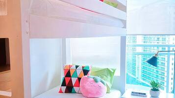 Un lit superposé avec une fenêtre, un bureau avec une lampe et une vue sur les immeubles.