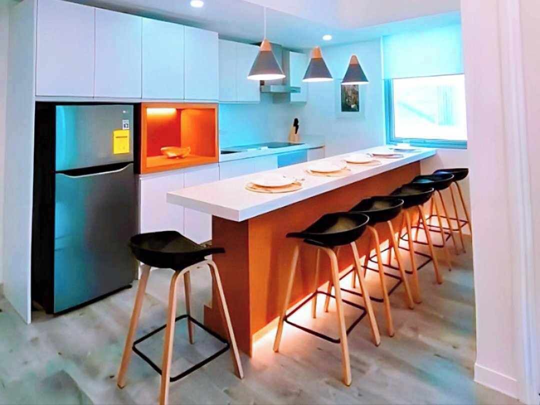 A modern kitchen with a central island, bar stools, and a refrigerator.