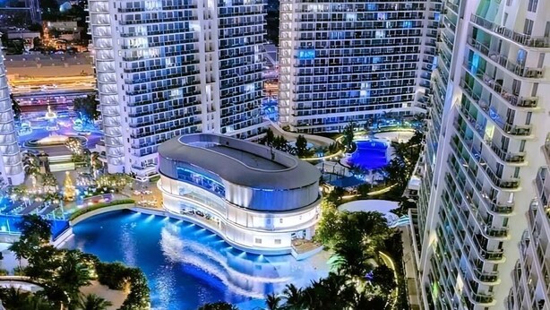 Un hôtel de grande hauteur doté de nombreux balcons, d’un espace piscine central agrémenté d’une cascade et entouré de verdure.