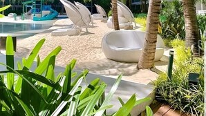 Un hôtel moderne doté d’une piscine, de palmiers et d’un espace extérieur aménagé pour se détendre.