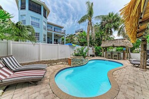 A swimming pool with lounge chairs, a thatched-roof structure, and a white fence. - Tuscan Tides - Custom Pool Home - powered by Island Real Estate (Holmes Beach)