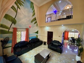 A spacious lobby with a high ceiling, a mural of palm trees, and a balcony with a metal railing.