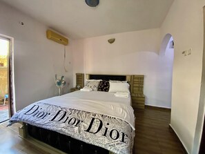 A bedroom with a bed covered in a Dior-themed blanket, a bedside fan, and a wooden headboard. - 6 Bedroom Serviced Apartments In House in Benin (Benin City)