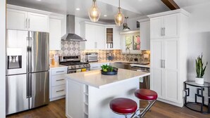 Una cocina moderna con armarios blancos, electrodomésticos de acero inoxidable y una isla central con taburetes.