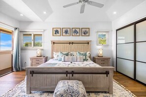 Une chambre à coucher avec un lit en bois, des tables de chevet, un ventilateur de plafond et des œuvres d’art encadrées accrochées au mur.