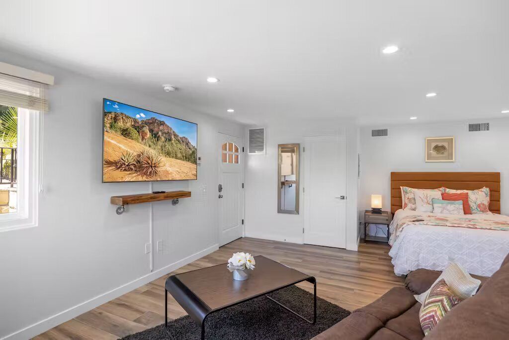 Une chambre à coucher moderne avec un grand lit, un téléviseur fixé au mur et une petite table de chevet.
