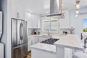 A modern kitchen with white cabinetry, a stainless steel refrigerator, a gas stove, and a window with blinds.