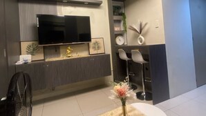 Ein modernes Wohnzimmer mit einem an der Wand befestigten Flachbildfernseher, einem Essbereich mit rundem Tisch und Stühlen sowie einem kleinen Beistelltisch mit Blumen in einer Vase.