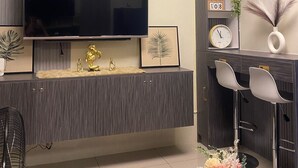 Ein modernes Wohnzimmer mit Flachbildfernseher an der Wand, einer integrierten Unterhaltungseinrichtung mit Dekorationsgegenständen, einer Uhr und einem kleinen Tisch mit Stühlen.
