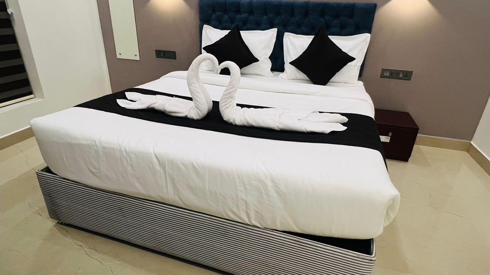 A neatly made bed with white linens and black pillows, a headboard with a tufted design, and a bedside table with a dark-colored box.