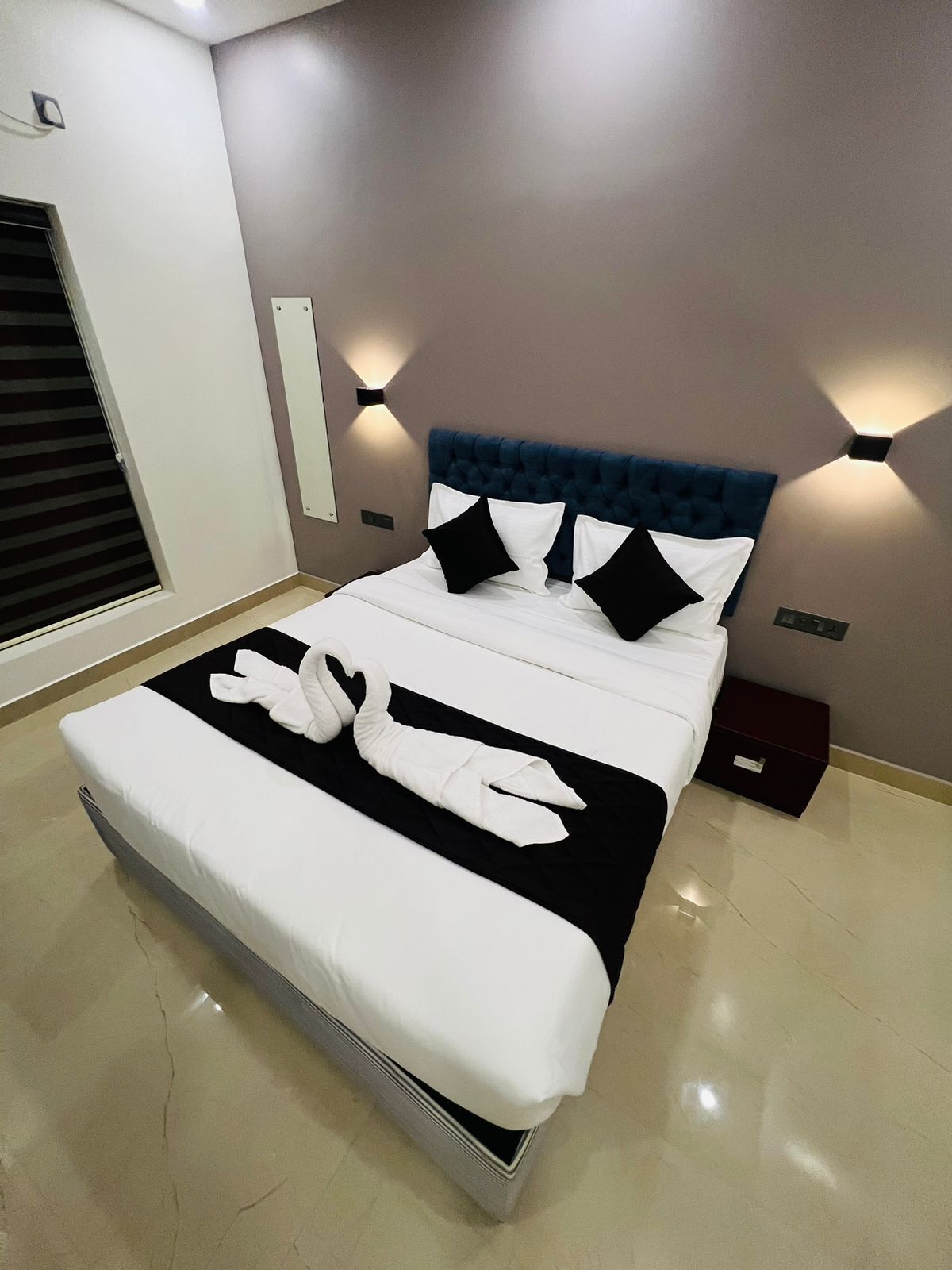 Ein modernes Hotelzimmer mit einem großen Bett, einem Kopfteil mit integrierter Beleuchtung und einem Nachttisch mit Schublade.