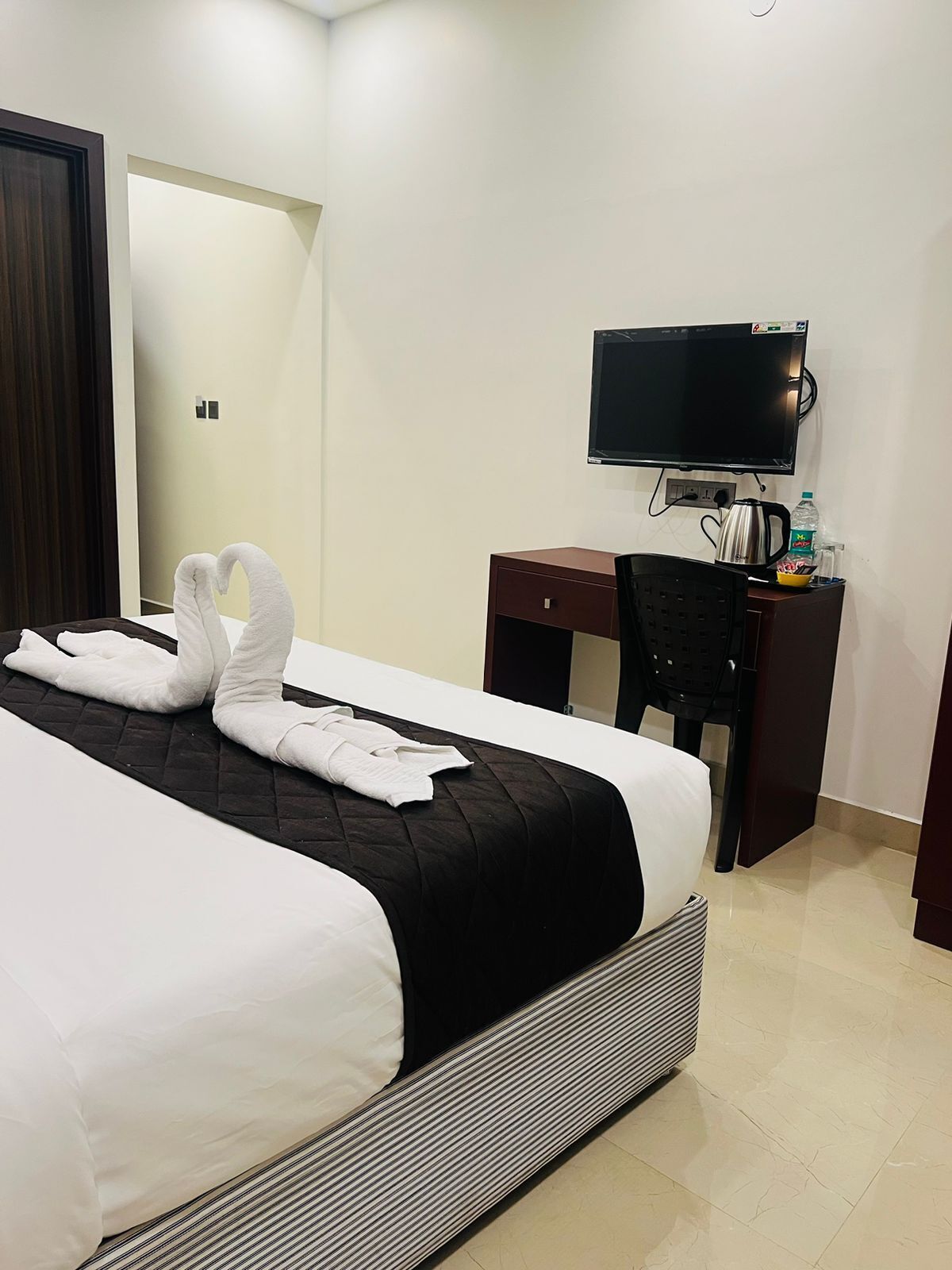 A hotel room with a bed, a desk, a chair, a television, and a kettle.