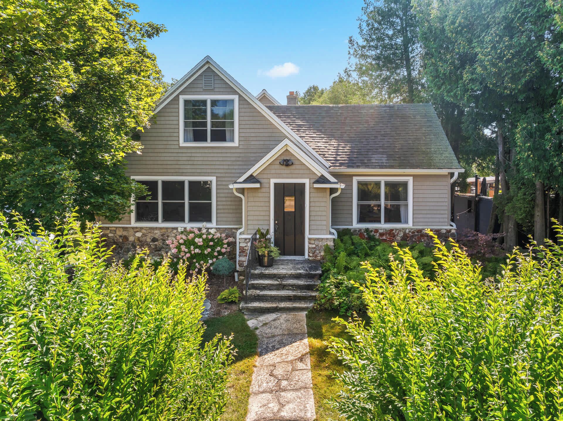 A two-story house with a stone pathway leading to the front door, surrounded by lush greenery.