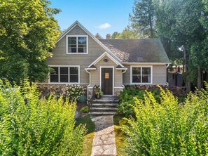 A two-story house with a stone pathway leading to the front door, surrounded by lush greenery. - Downtown Baileys Harbor Waterfront: Limestone Edge (Baileys Harbor)