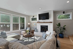 A living room with a fireplace, a television mounted above it, and large windows. - Downtown Baileys Harbor Waterfront: Limestone Edge (Baileys Harbor)
