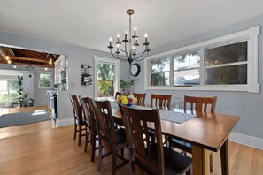 A dining area with a wooden table, chairs, a chandelier, and a clock on the wall. - Downtown Baileys Harbor Waterfront: Limestone Edge (Baileys Harbor)
