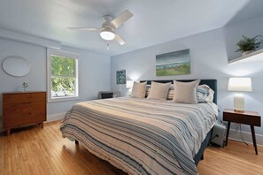 A bedroom with a bed, a ceiling fan, a window, a dresser, a bedside table, and a lamp. - Downtown Baileys Harbor Waterfront: Limestone Edge (Baileys Harbor)