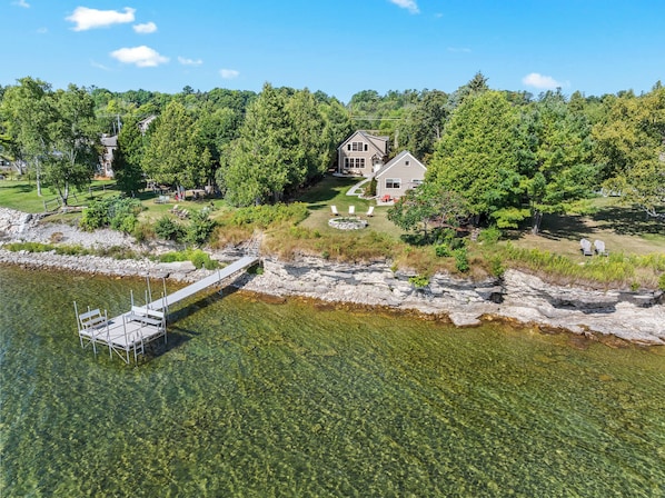 A lakeside property with a dock, clear water, and a house surrounded by trees. - Downtown Baileys Harbor Waterfront: Limestone Edge (Baileys Harbor)