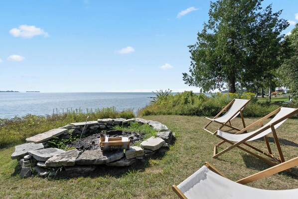 A stone fire pit with two lounge chairs and a view of the water. - Downtown Baileys Harbor Waterfront: Limestone Edge (Baileys Harbor)