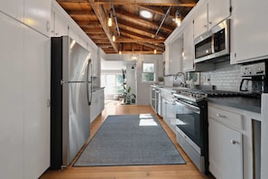 A modern kitchen with stainless steel appliances, wooden ceiling beams, and a view to the outside.