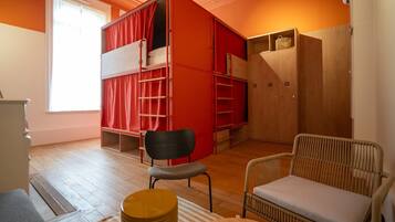 A room with a bunk bed, a chair, a sofa, and a wooden wardrobe.