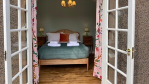 Une chambre à coucher avec un lit en bois, une couvre-lit verte, des oreillers blancs et un lustre. Il y a deux tables de chevet avec des lampes.