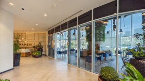 Un moderno vestíbulo de hotel con una mesa de recepción, puertas de vidrio que dan a un comedor y plantas en macetas.